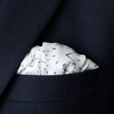 Watch dial design silk pocket square with white background and blue and grey watch dials folded in top pocket of navy blue jacket.